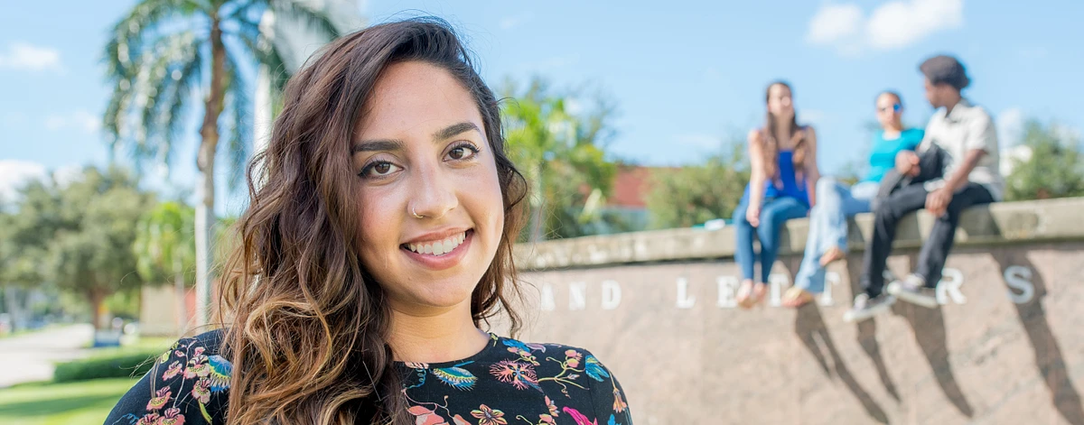 A student stands smiling in front of an entrance to campus